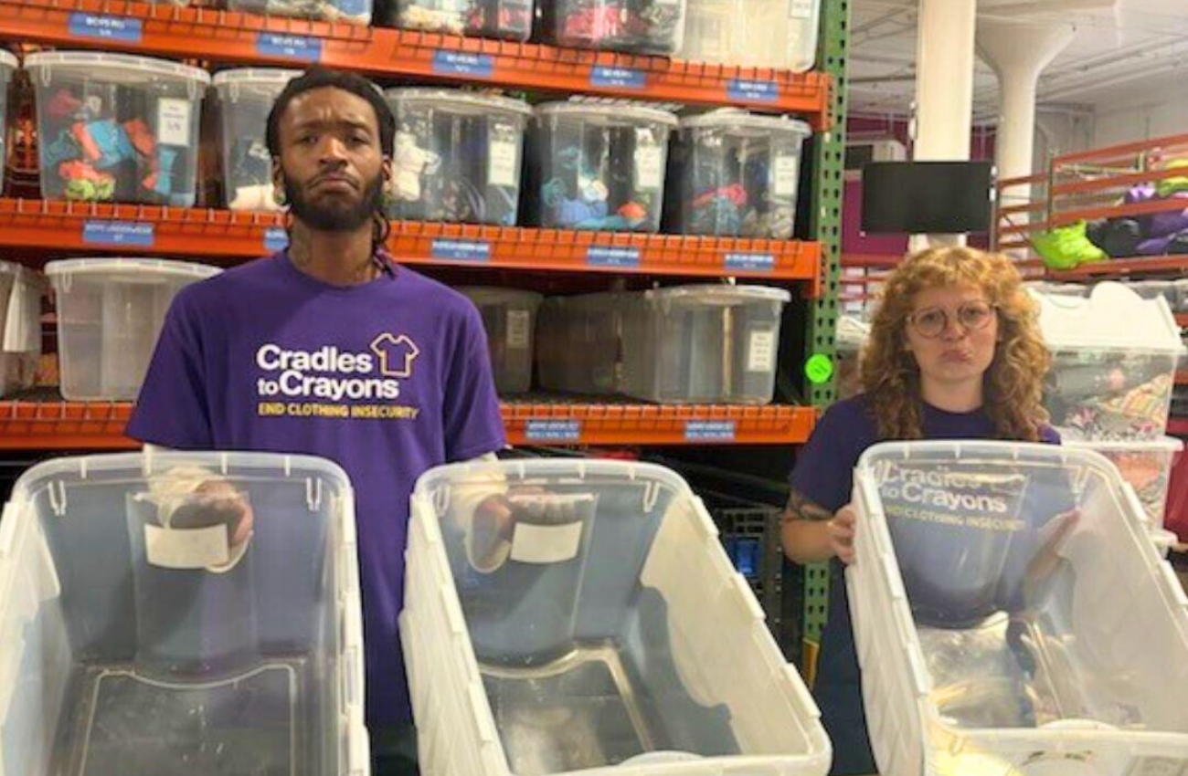 Cradles to Crayons volunteers holding up empty clothing bins