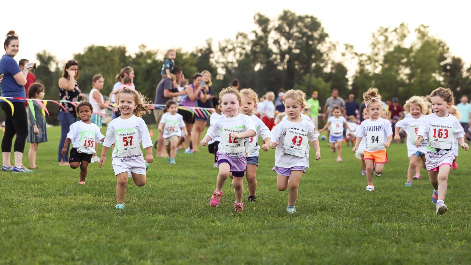 Tiny children running in a race on green grass.