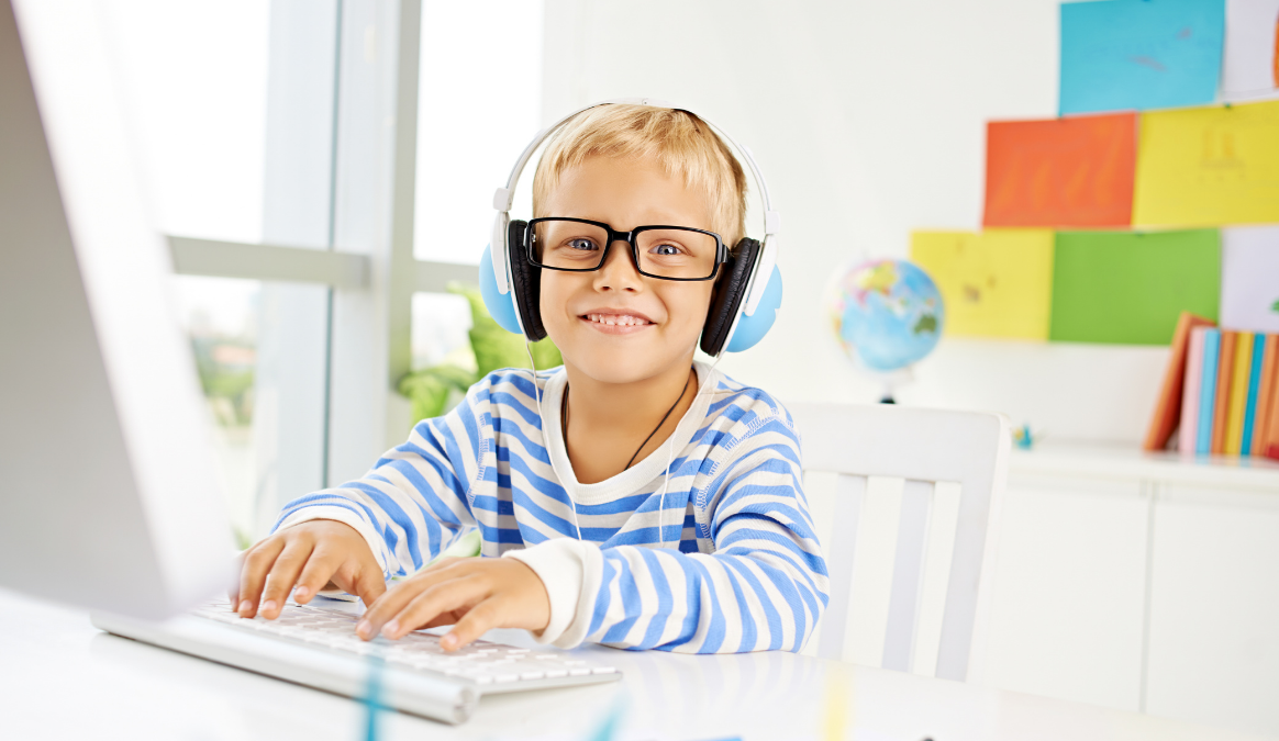 Little boy smiling with headphones at his PC computer.
