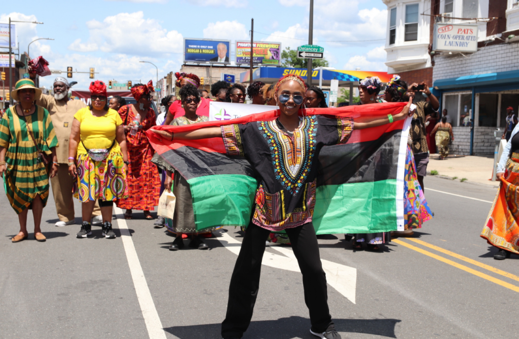 Juneteenth parade on Philadelphia street featuring a woman holding a Black culture flag draped on her shoulders