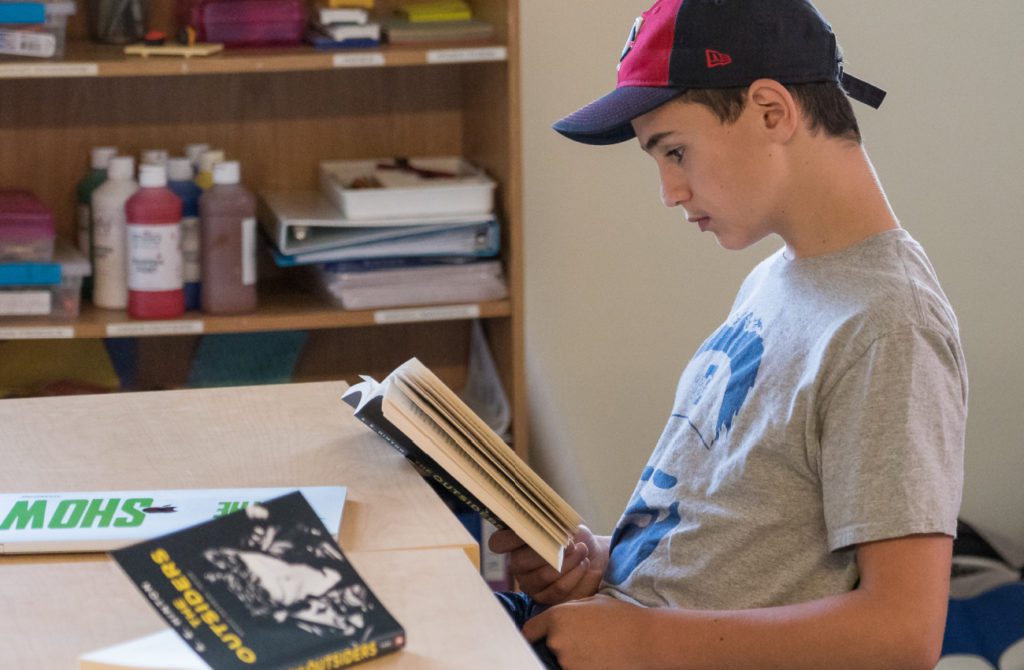 teenage boy at a desk reading a book