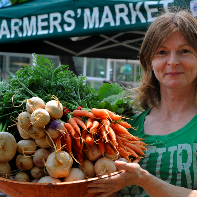 A womn holds a basket of fresh produce for sale at a farmer's market