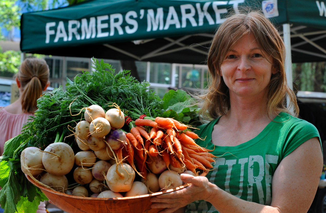 A womn holds a basket of fresh produce for sale at a farmer's market