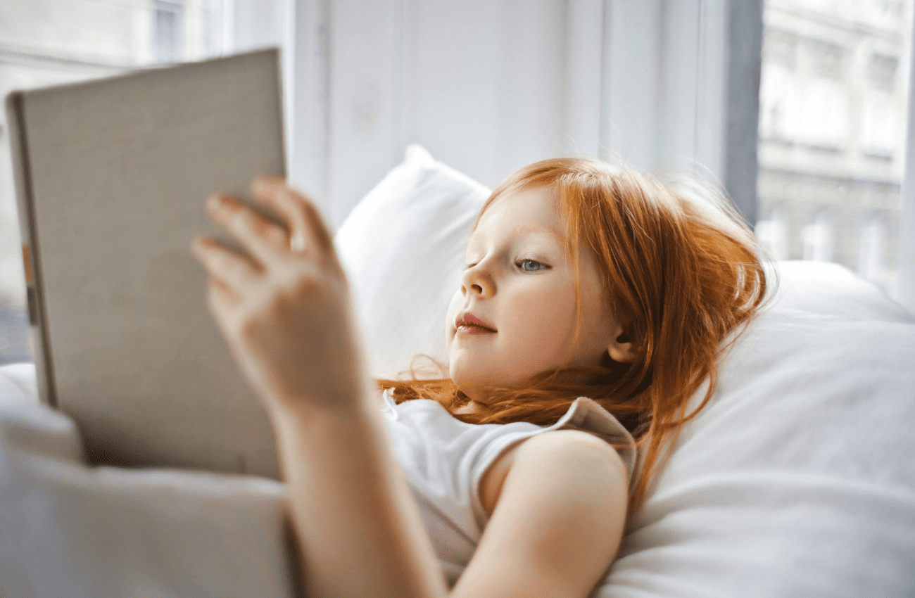 Young girl reading in bed during the summer.