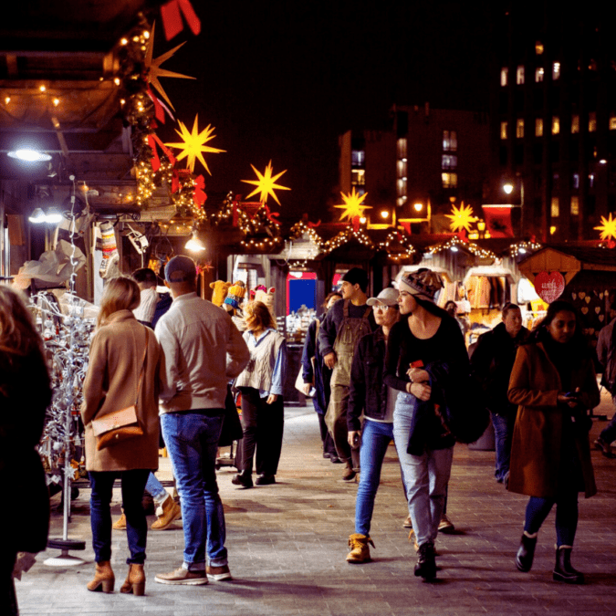 People stroll at night among twinkling lights at Christmas Village in Philadelphia, a holiday market.