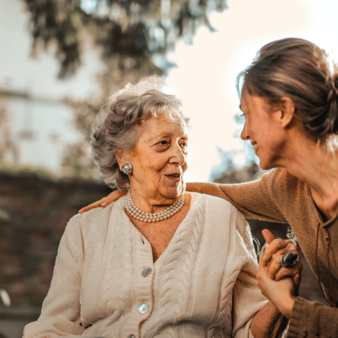 Older mother aging parent and adult daugher hold hands and smile at each other
