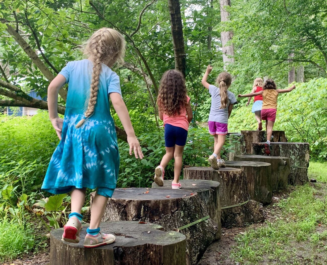 young children walking across tree stumps outdoors