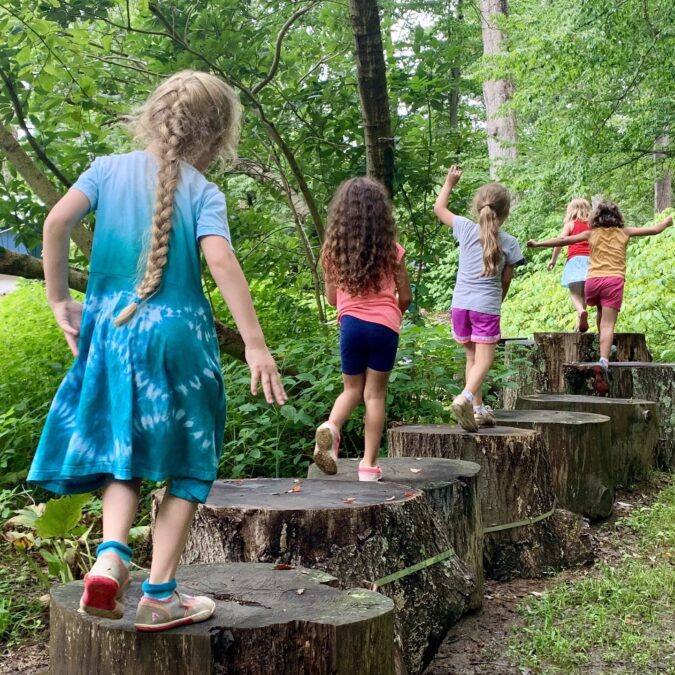 young children walking across tree stumps outdoors