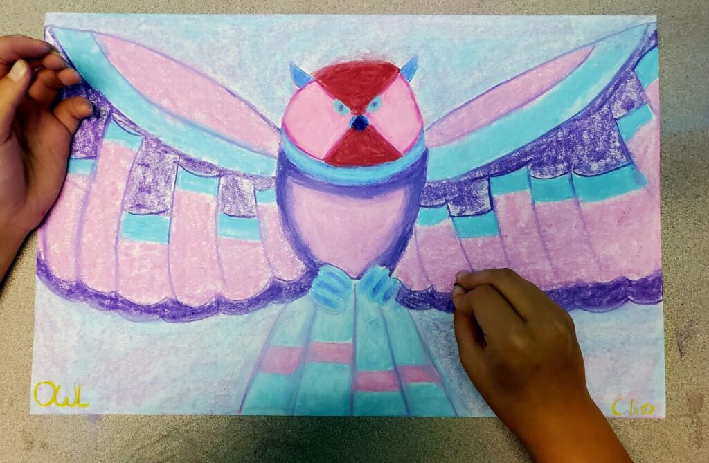 child's hands drawing a colorful owl