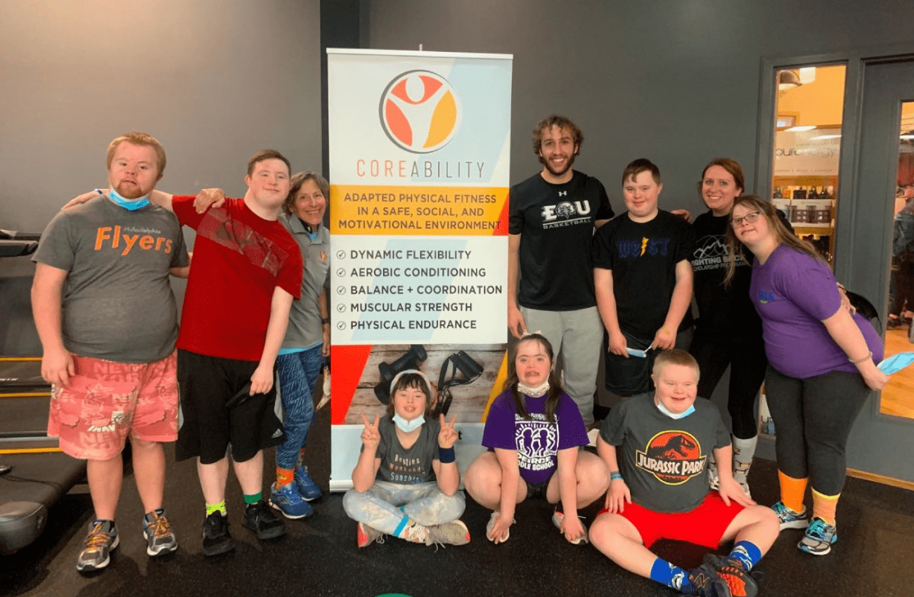 A group of kids and young adults in an inclusive fitness class pose for a photo with their CoreAbility trainer.