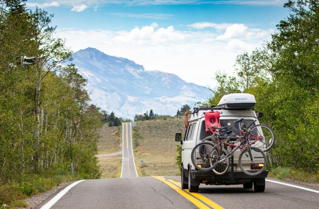 A family camper van with bikes drives on a scenic road.