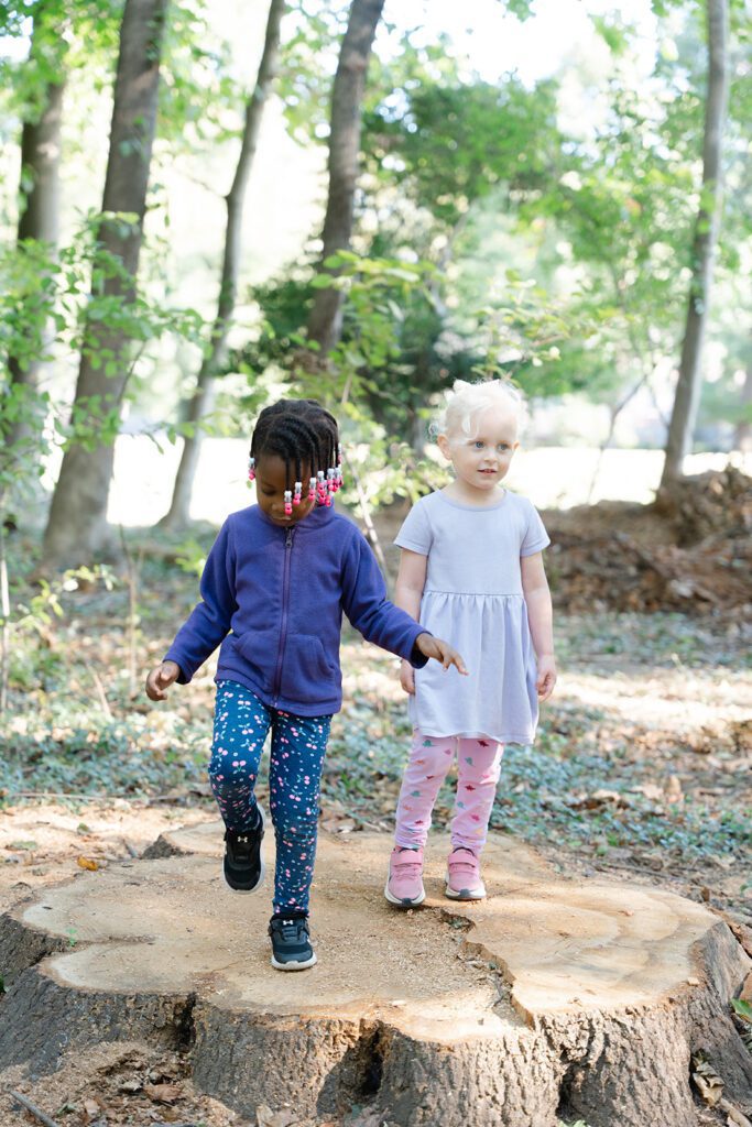 Two preschool children exploring nature and climbing on a large tree stump