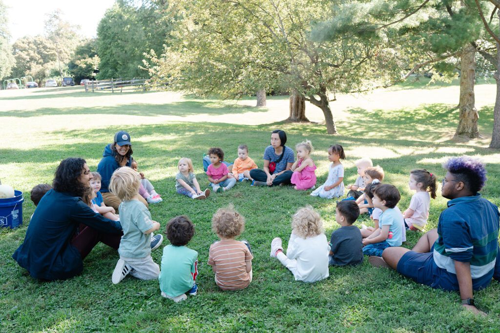 Preschool students and teachers gathering in a circle outdoors in nature for a lesson