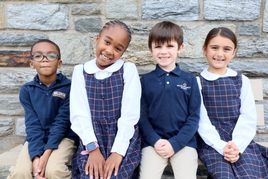 Waldron Mercy students sitting on a bench in their school uniforms.