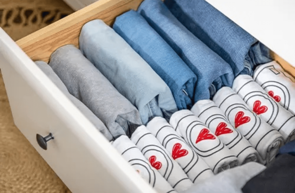 A home organizer from Lessen the Loads opens a dresser drawer with neatly folded jeans and t-shirts with red hearts. 