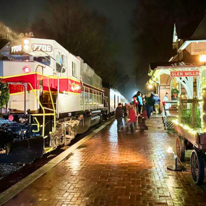 A holiday train decorated with wreath sits beside a train station in Glen Mills, decked out in lights.