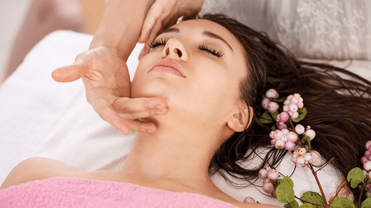 Tranquil scene in a spa of a woman with pink towel and flowers getting a facial to optimize wellbeing.