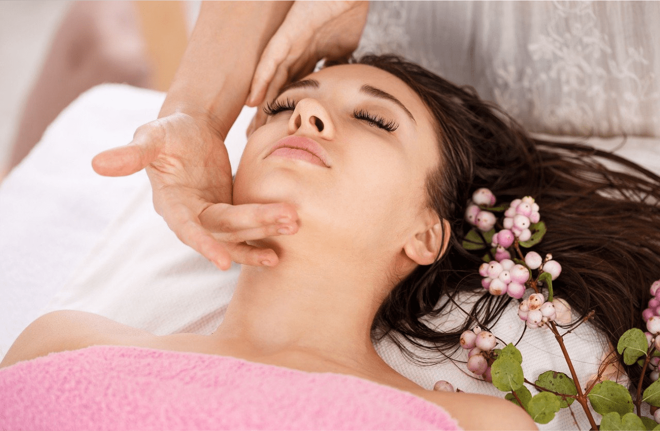 Tranquil scene in a spa of a woman with pink towel and flowers getting a facial to optimize wellbeing.