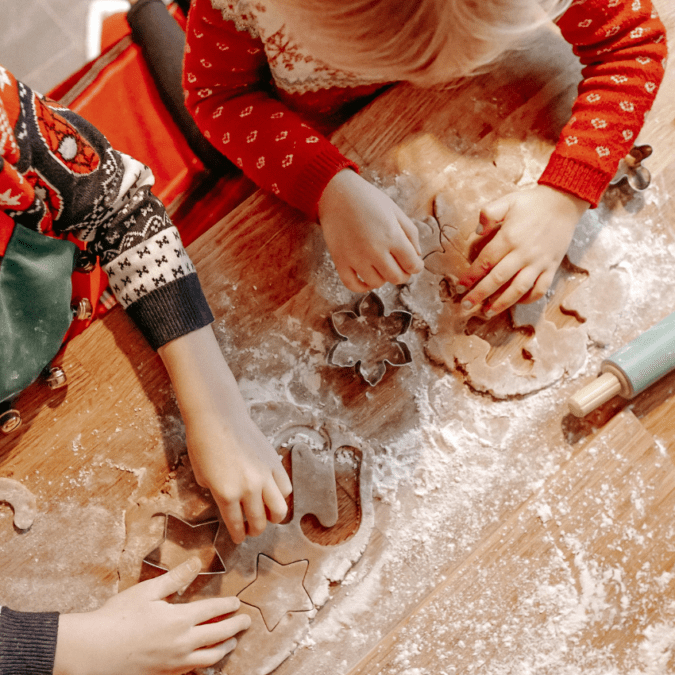 Two little children in Christmas sweater are engaged in holiday cookie baking.