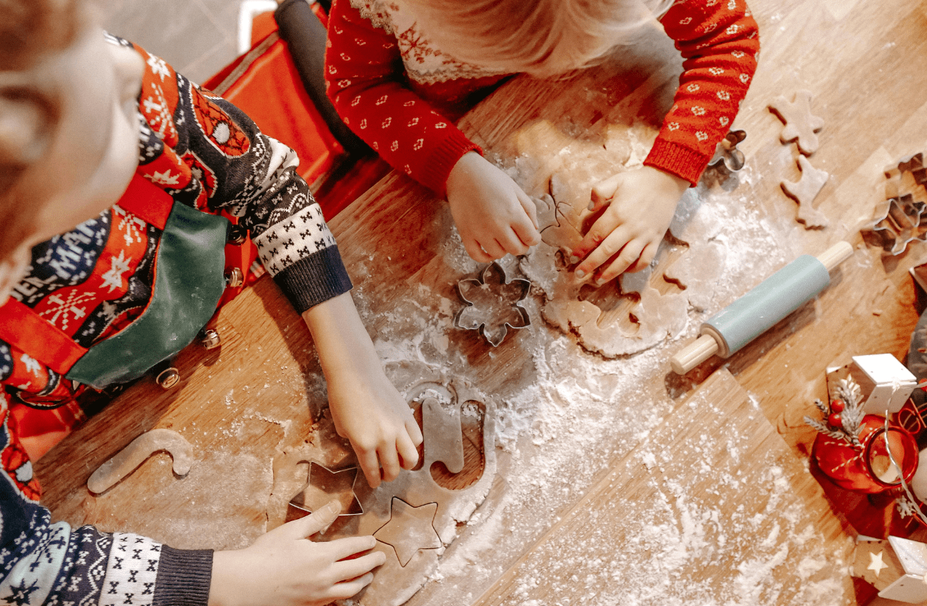 Two little children in Christmas sweater are engaged in holiday cookie baking.
