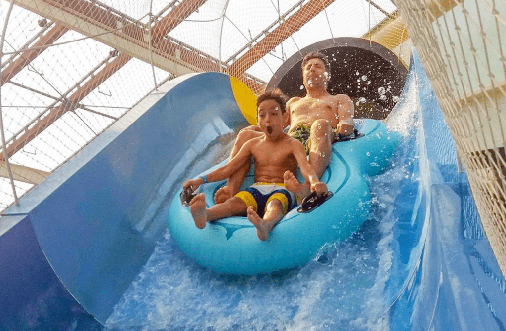 Father and son ride a steep water slide at Aquatopia, an indoor water park.