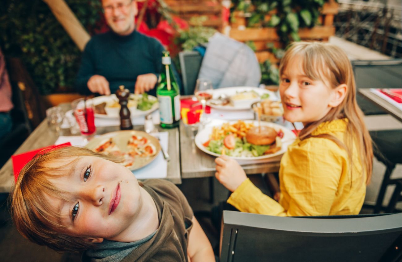 A father and two elementary school children at a restarurant table with pizza, and burgers and fries.