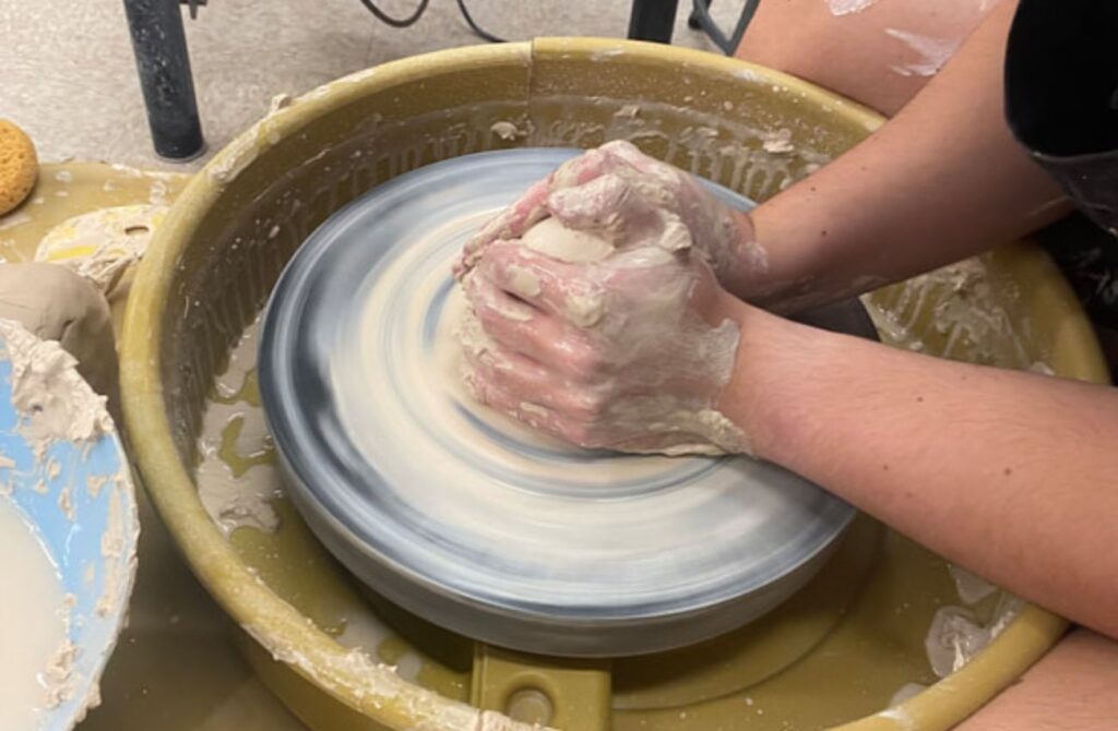 Young hands shape a clay form on a spinning pottery wheel in a youth arts class at Chester County Art Association.