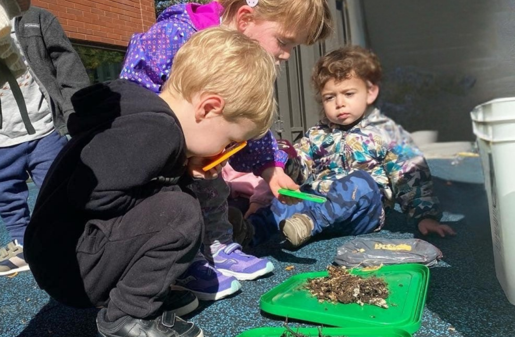 preschool students look at mulch and dirt under a magnifying glass