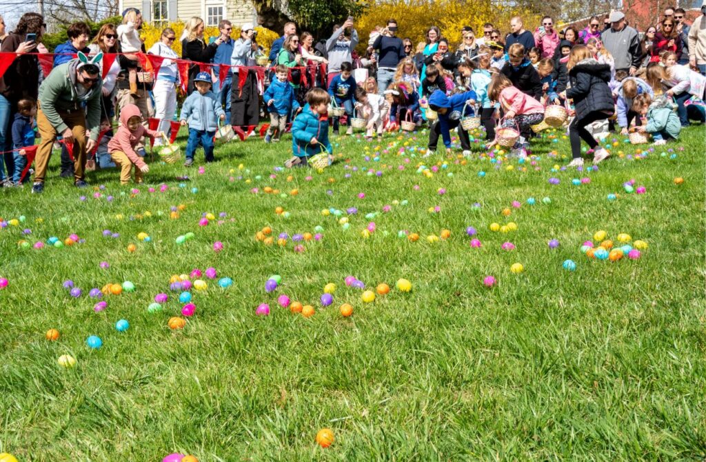 Kids with baskets scramble to pick up the many colored eggs in the grass while parents watch. 