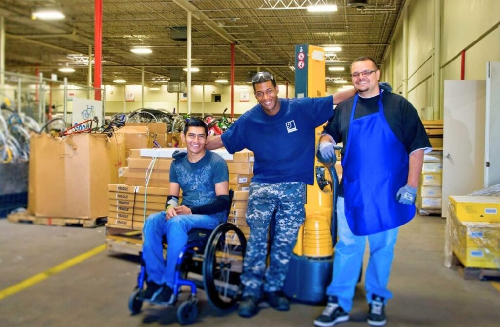 A man in a wheelchair poses with two other employees in a warehouse of Goodwill Inc., a Main Line inclusive hiring resource. 