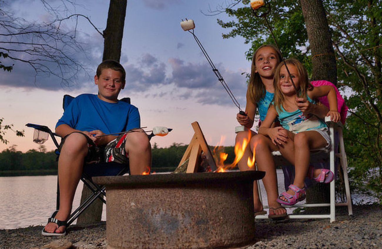 Three kids of varying ages roast marshmallows around the campfire after sunset.