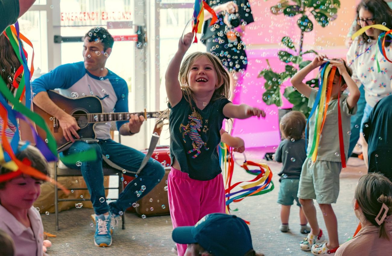 Mister John's Music plays guitar at a kids party with bubles and rainbow pom-poms.