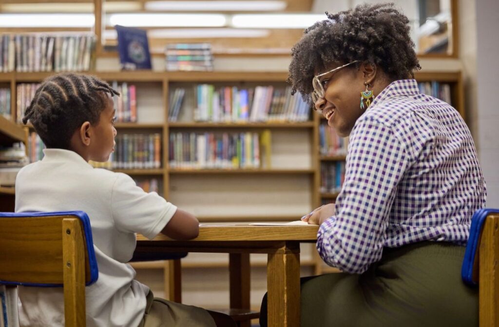 A female educator smiles at a young boy in the Benchmark School library. 