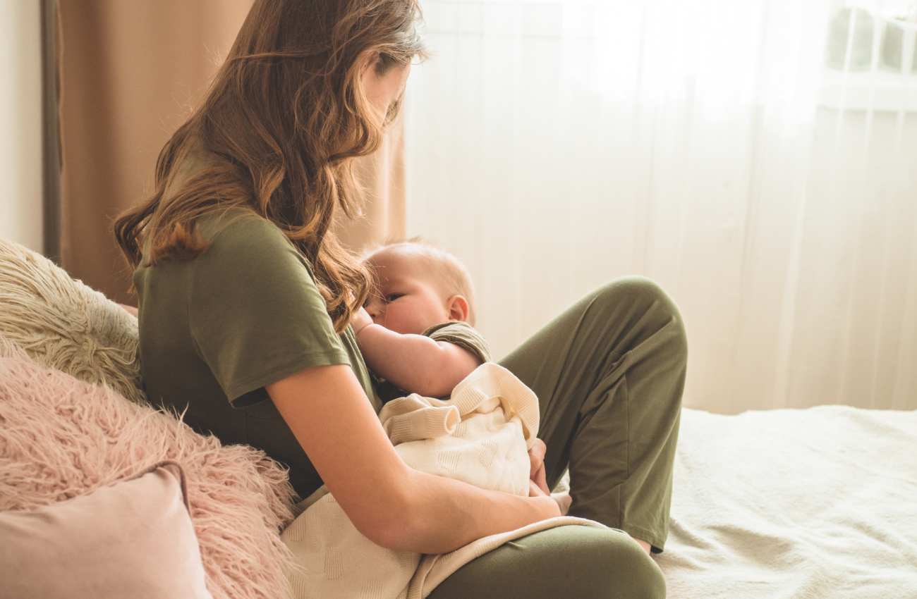 A mom sits against fuzzy pillows while breastfeeding her baby.