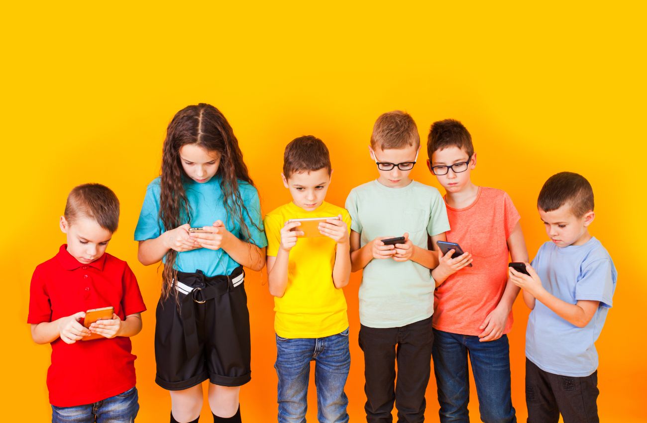 Six elementary school kids look at screens against a yellow wall.