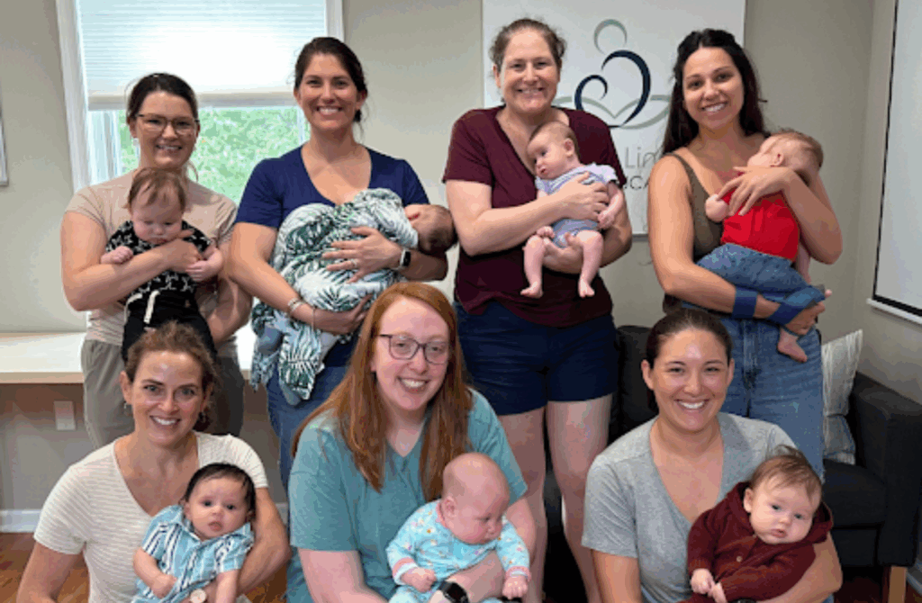 New moms hold their infants and smile for the camera at a breastfeeding support class. 