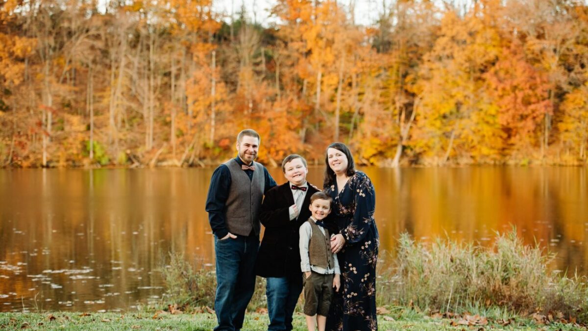 The Thomas family with their two young boys in front of a lake with fall foliage