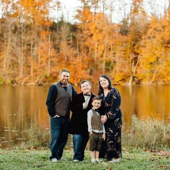The Thomas family with their two young boys in front of a lake with fall foliage