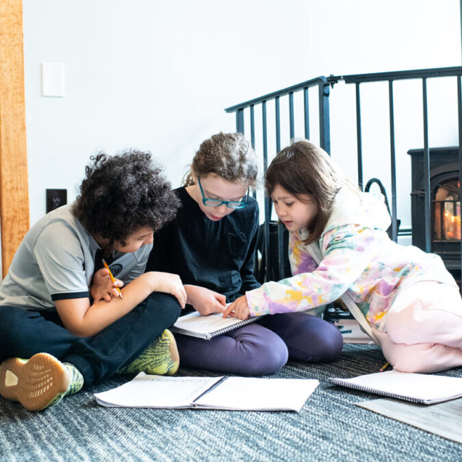 Gladwynne Montessori students working together on a project on the carpet in their classroom, warmed by a fireplace