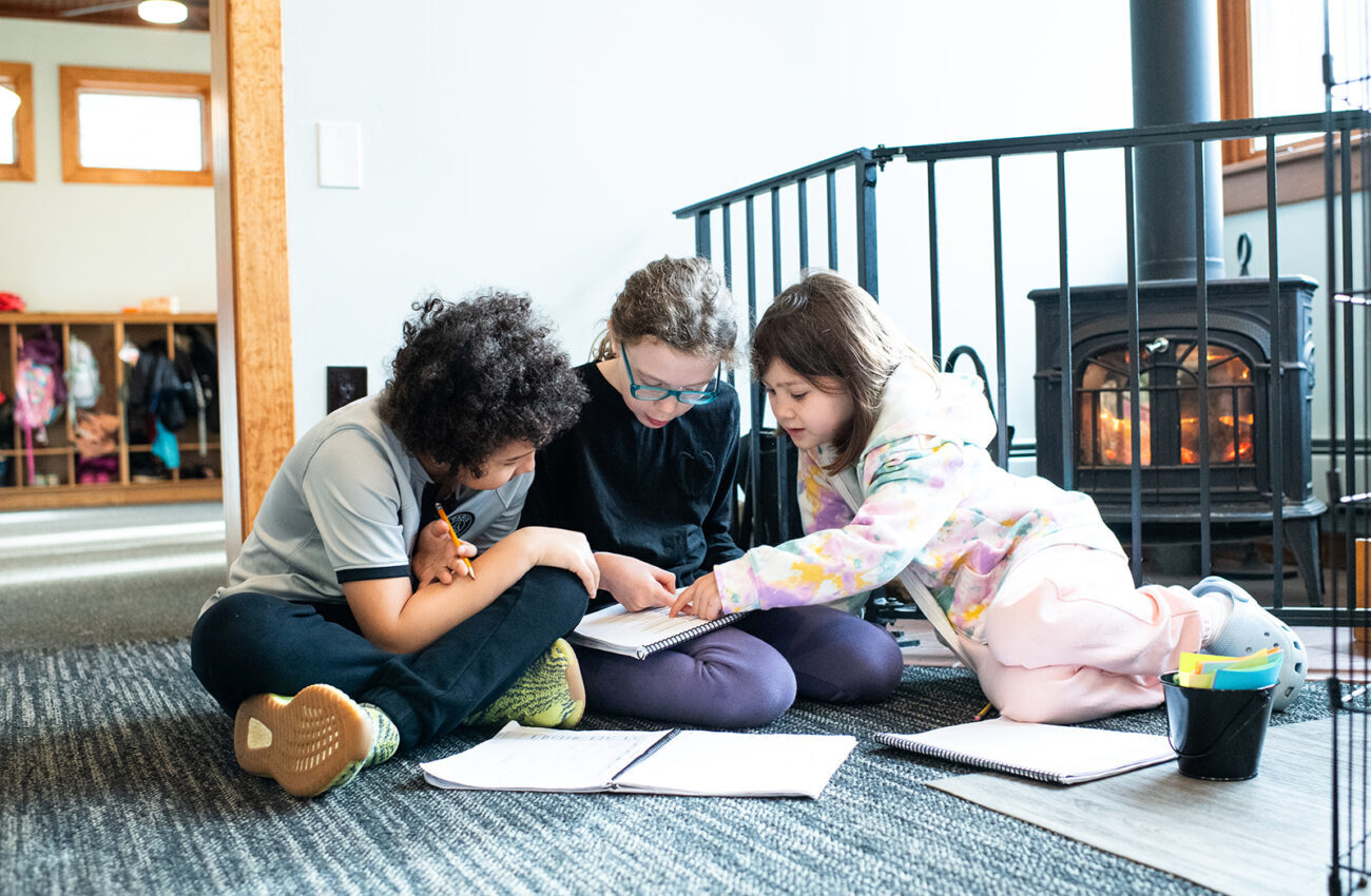 Gladwynne Montessori students working together on a project on the carpet in their classroom, warmed by a fireplace