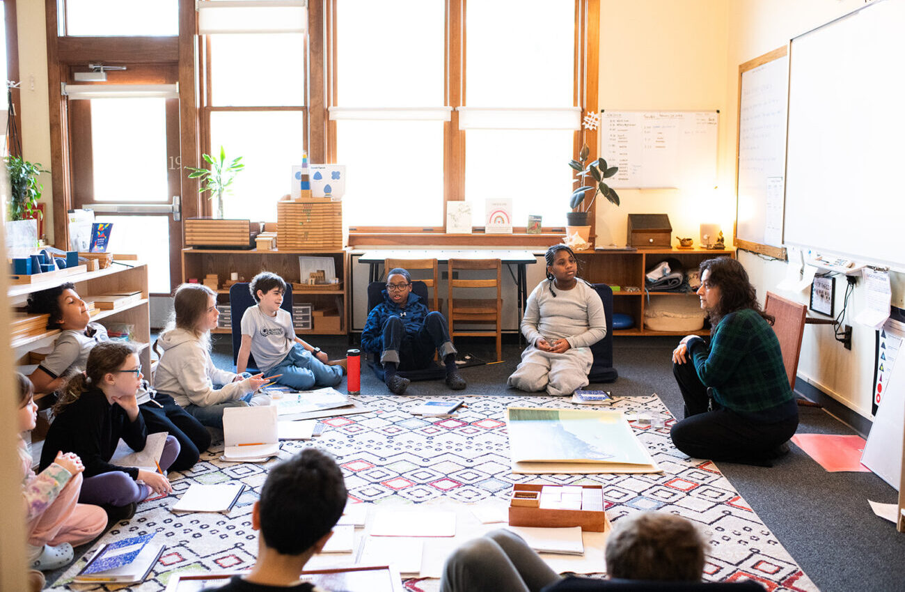 Students at Gladwyne Montessori sitting with their teacher on the carpet while learning a lesson, these are middle school students.