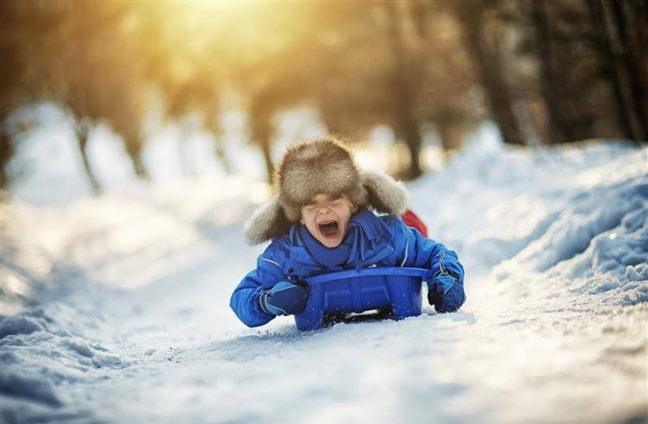 Young child sledding with trees behind him, healthy holiday season article