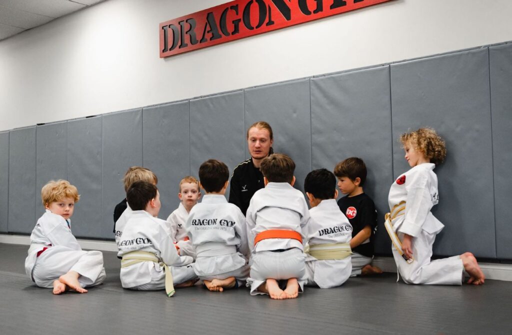 A group of little boys sit around their martial arts teacher on the mat.