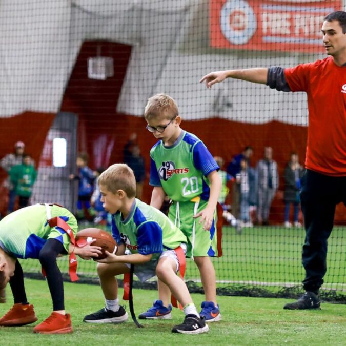 Little boys practice football plays with a coach at a winter sports class.