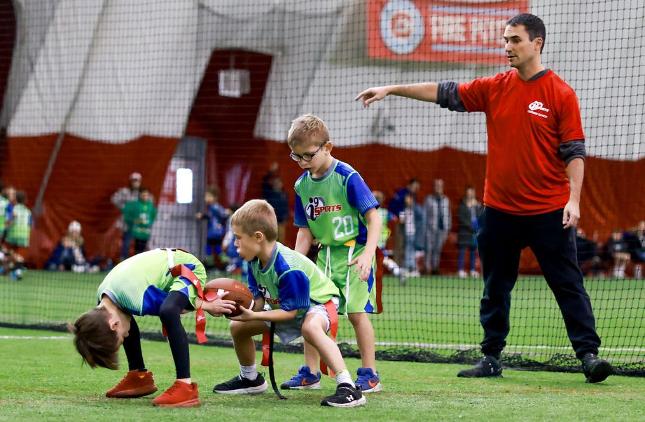 Little boys practice football plays with a coach at a winter sports class.
