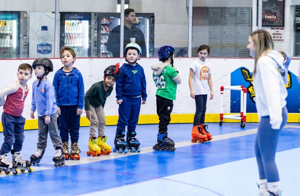 A day camp guide lines up seven young school boys in rollerblades and roller skates inside a rink.