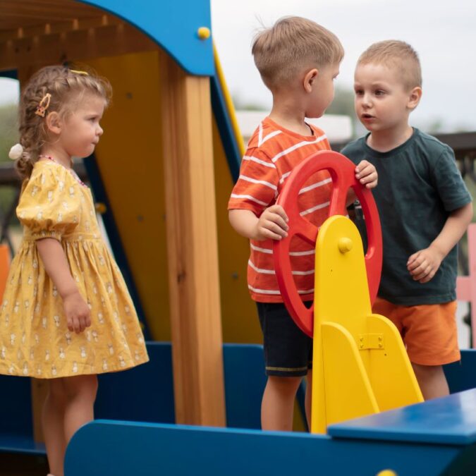 A young boy looks menacingly at another boy on play equipement while a little girl looks on.