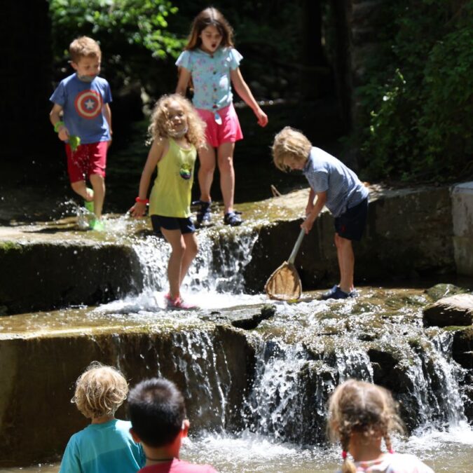 Young kids splash in a woodsy waterfall at Riverbend Nature Camp.