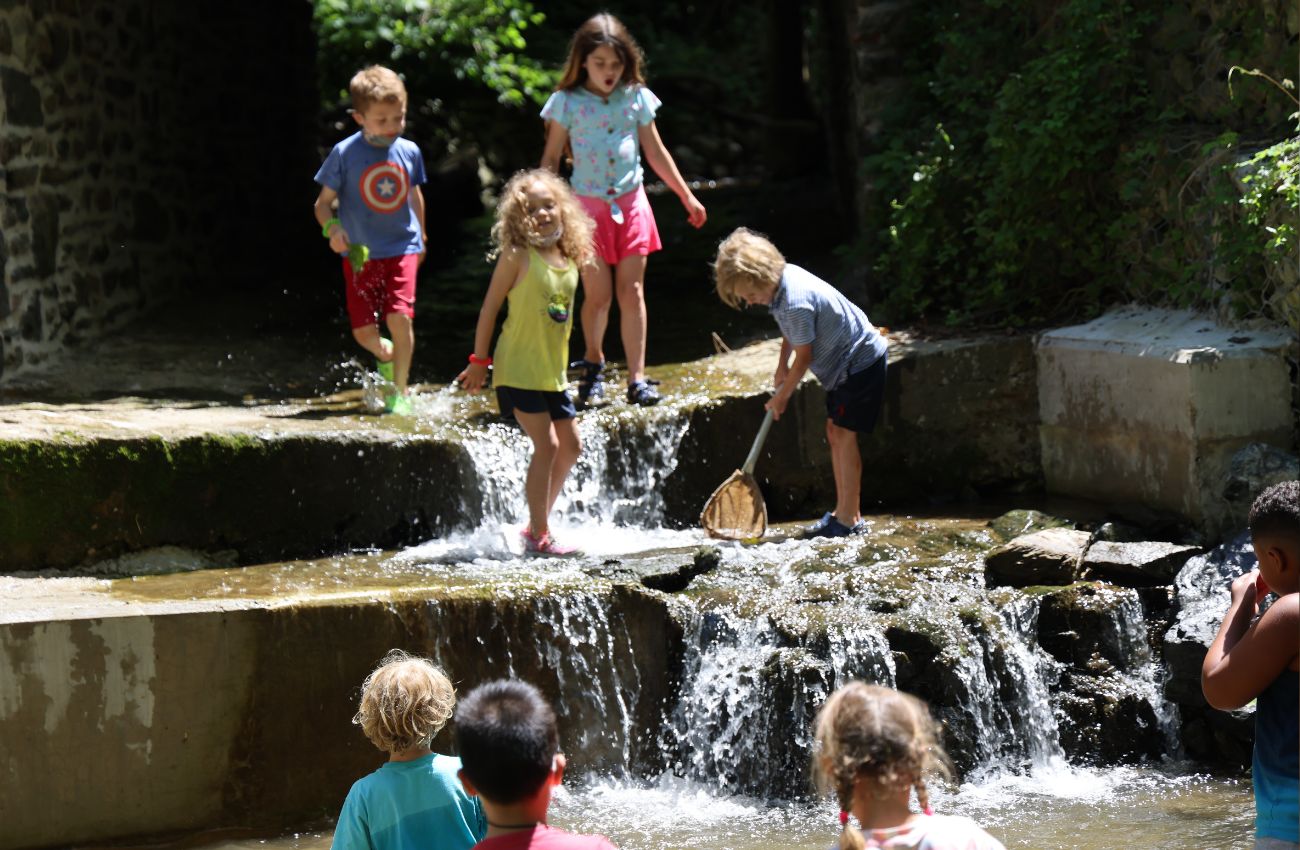 Young kids splash in a woodsy waterfall at Riverbend Nature Camp.