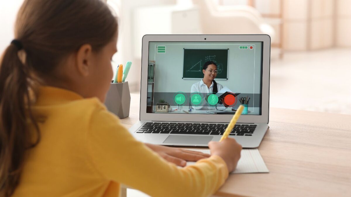 A young girl practices homework with the help of an online tutor on her laptop.